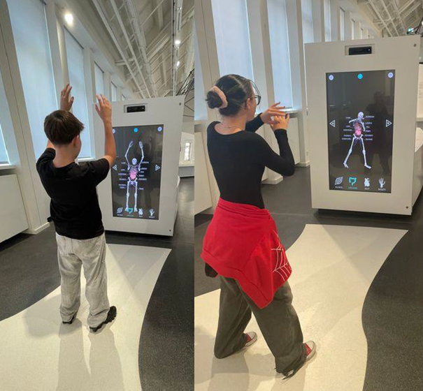 Foto zweier Schüler die ein interaktives Museumstück ausprobieren. Ein Scanner, der Skelett und die eigene Anatomie erklärt.